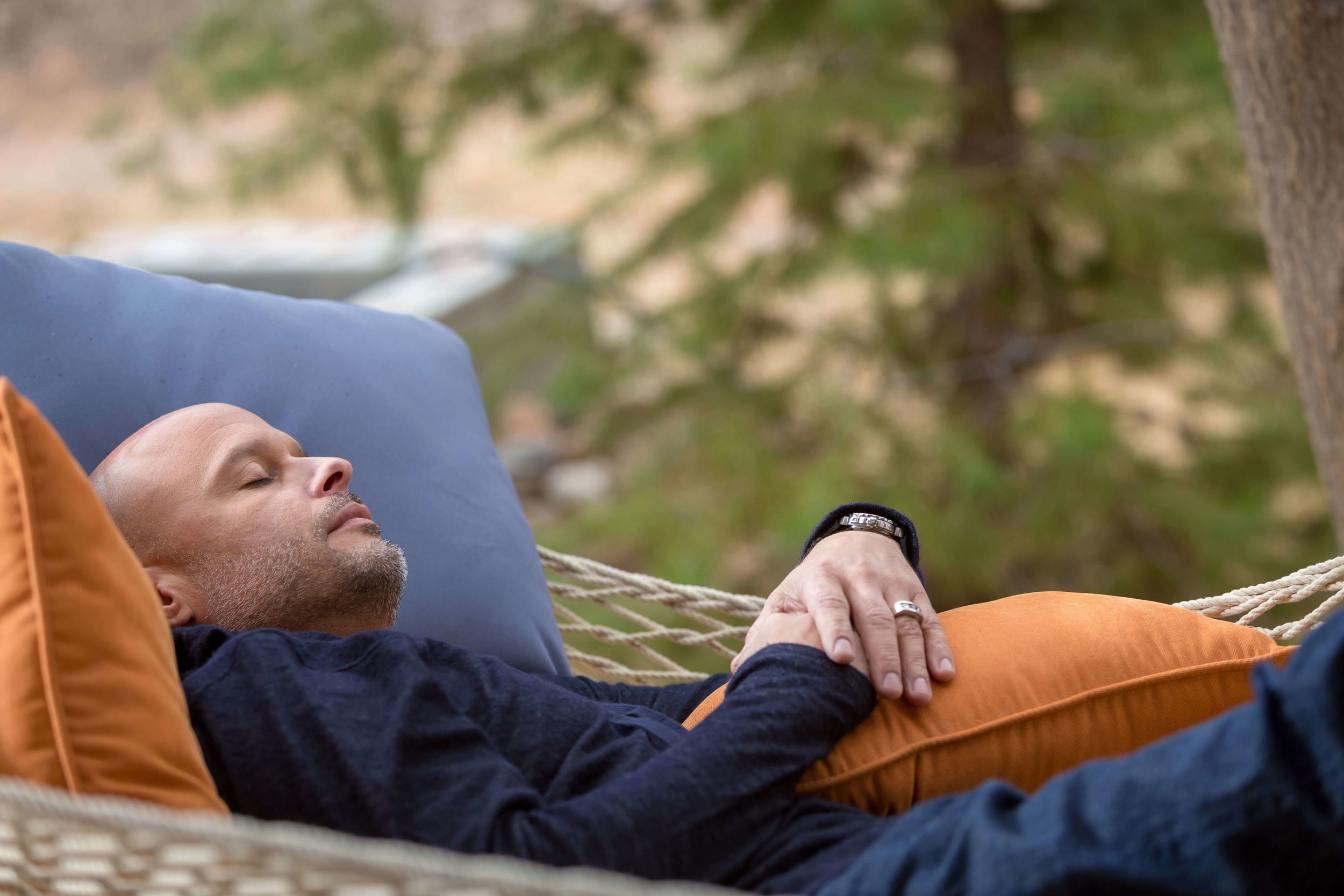 A man laying down in a hammock holding a pillow with his eyes closed