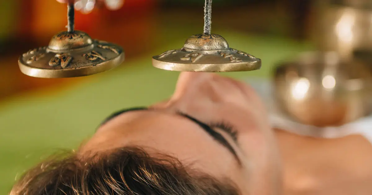 a woman is laying down with her eyes closed and a person is holding a pair of bells over her head